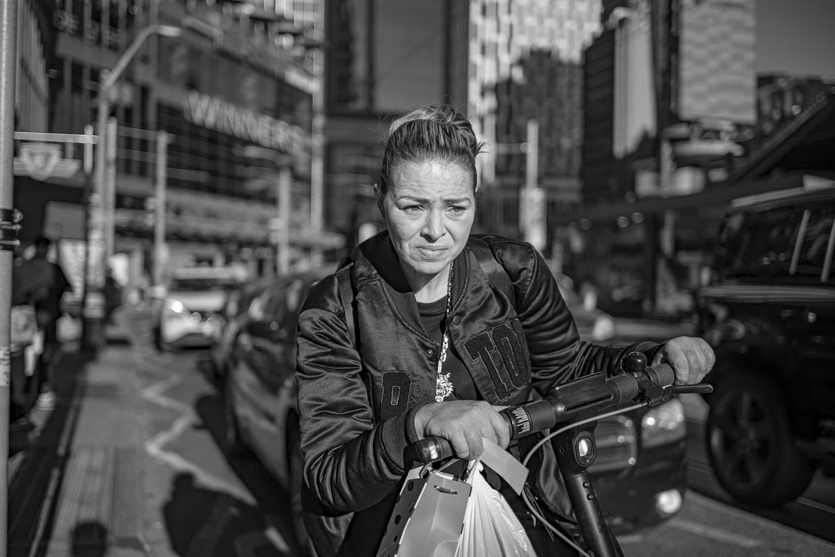 A woman holding a scooter on a sunlit Toronto street