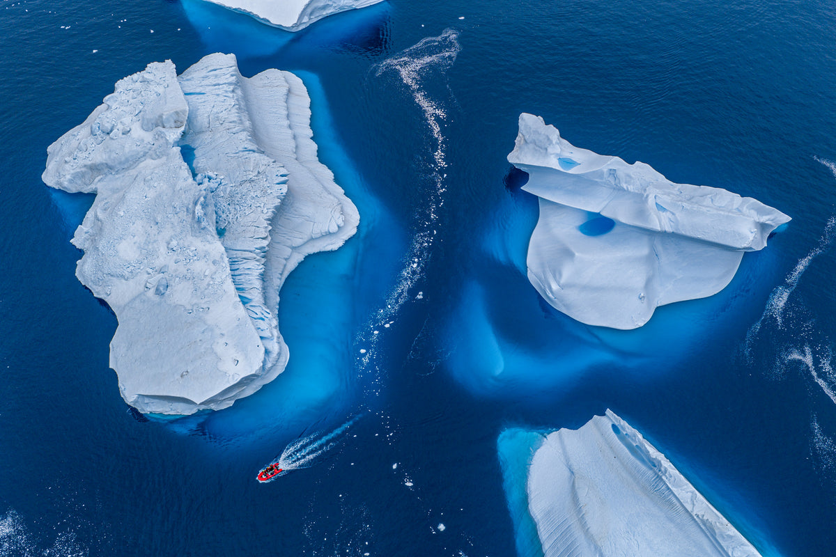 An aerial view of a red Zodiac moving between blue Antarctic icebergs