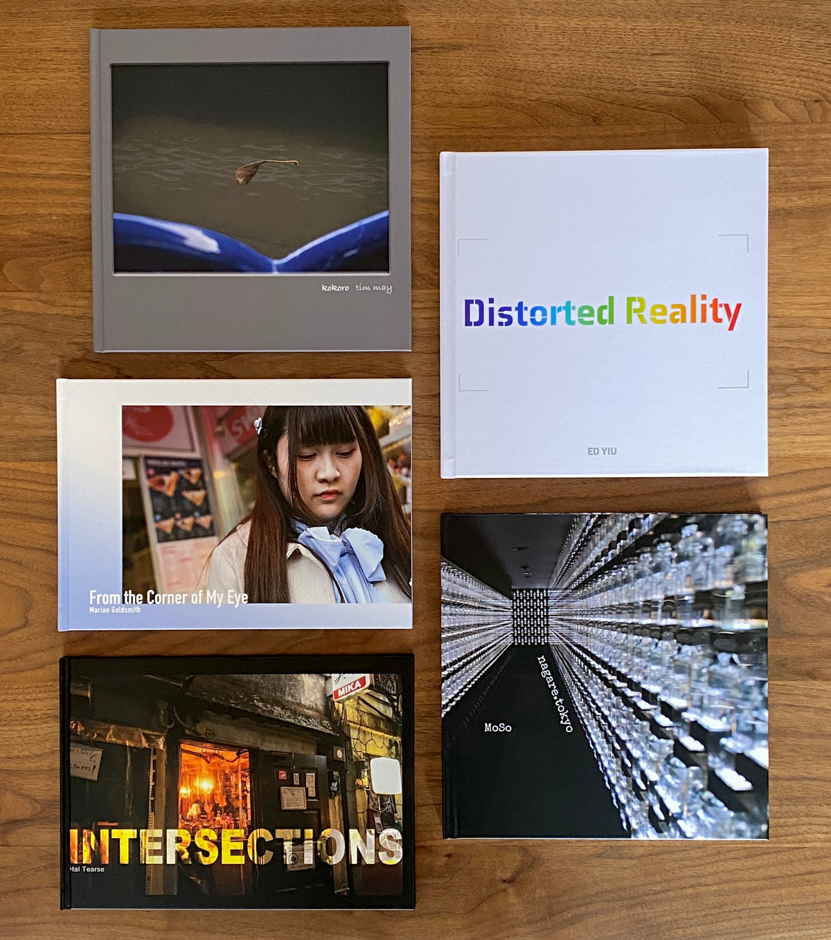 Five photographic books arranged on a wooden table, including Distorted Reality, From the Corner of My Eye, and Intersections