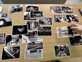 Black-and-white photographic prints spread across a wooden table, with a hand moving one print during an edit.