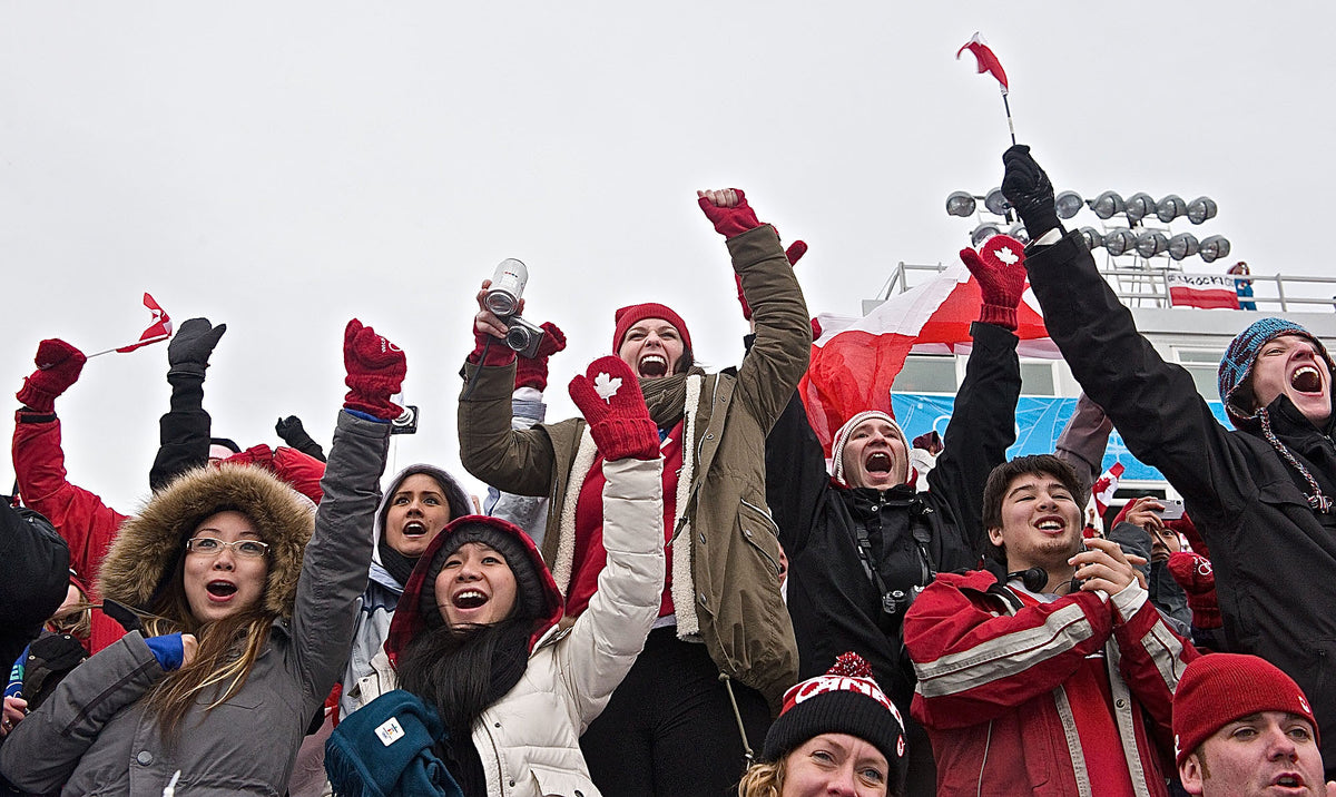 A cheering crowd waving Canadian flags and raising their arms.